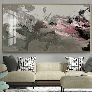 May include: Abstract painting with gray, black, and pink brushstrokes. The painting is framed in a gold frame and is hanging on a wall above a couch.