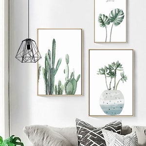 May include: Three framed watercolor paintings of plants. The first painting features a large green monstera leaf. The second painting features a group of cacti in shades of green. The third painting features a succulent plant in a blue and white pot.