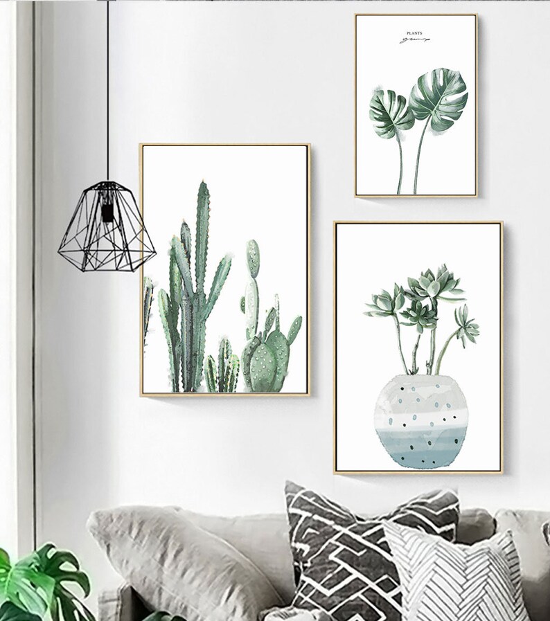 May include: Three framed watercolor paintings of plants. The first painting features a large green monstera leaf. The second painting features a group of cacti in shades of green. The third painting features a succulent plant in a blue and white pot.
