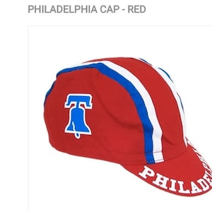 May include: Red cycling cap with white and blue stripes and a Liberty Bell logo. The cap has the word "PHILADELPHIA" written on the brim.