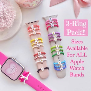 May include: Three sets of colorful beaded rings with letter and heart charms, displayed on Apple Watch bands. The text "3-Ring Pack!!!" and "Sizes Available For ALL Apple Watch Bands" is visible in the image.
