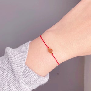 May include: A red string bracelet with a single brown bead.
