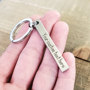 May include: Silver keychain with a rectangular tag that says "Your custom text here".