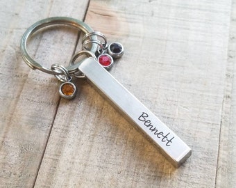 May include: Silver keychain with a bar charm engraved with the name "Bennett". The keychain has a silver ring and three small colorful crystal charms.