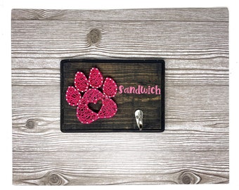 May include: A wooden sign with a pink string art paw print and a heart in the center. The sign has a metal hook and the text "Sandwich" written on it.