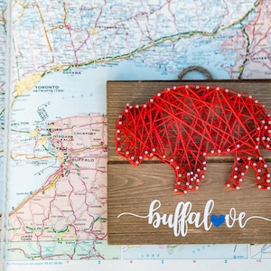 May include: Red string art of a buffalo on a wooden plaque with the text "buffalove" in white with a blue heart.