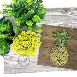 May include: A wooden sign with a string art pineapple design. The pineapple is made with yellow and green yarn. The sign is on a whitewashed wood background.