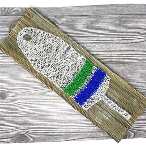 May include: A white, green, and blue string art buoy on a wooden background.