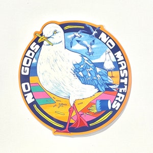 Puede incluir: Una pegatina redonda con fondo azul y naranja. La pegatina presenta una gaviota blanca con un ala azul, sosteniendo una papa frita en su pico. El texto "NO GODS NO MASTERS" está escrito en un círculo alrededor de la gaviota.