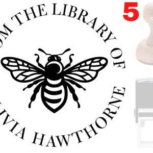 May include: A black and white bee illustration with wings spread, inside a circle with the text "From the Library of Olivia Hawthorne". The circle is surrounded by a white background. The image is a design for a self-inking rubber stamp.
