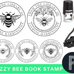 May include: Four black and white round rubber stamps with the text "From the Library of Jasmine Harrington" and a bee design. The stamps are shown with a self-inking stamp and a wooden handle stamp. The text "Buzzy Bee Book Stamp" is shown in green letters on a white background.