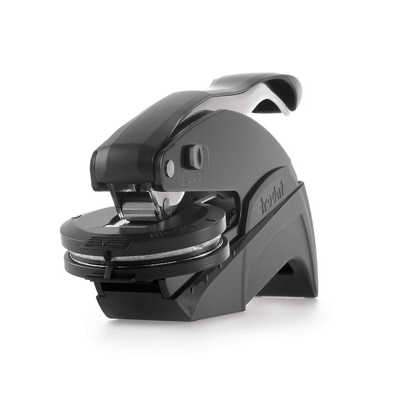May include: A black Trodat embosser with a handle and circular die. The embosser is made of plastic and metal. The die has the words "UP SIDE" printed on it. The embosser is designed to create raised impressions on paper.