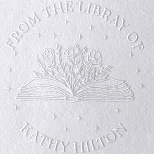 May include: White embossed stamp with the text "From the Library of Kathy Hilton" and a design of an open book with flowers growing from it.