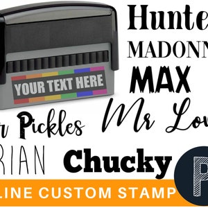 May include: A black and gray self-inking stamp with a rainbow stripe design and the text "YOUR TEXT HERE". The image also shows several examples of custom text that can be used with the stamp, including "Hunter", "MADONNA", "MAX", "Mr Pickles", "Mr Love", "BRIAN", "Chucky", and "P". The text "1 LINE CUSTOM STAMP" is also visible.