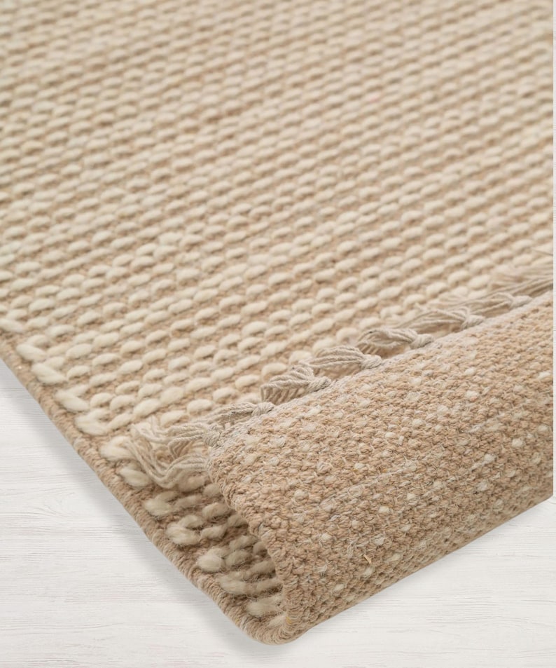 Peut inclure: Gros plan d'un tapis tiss&eacute; beige et blanc avec une bordure &agrave; franges. Le tapis est roul&eacute;, montrant la texture du tissage.
