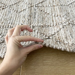 May include: Close-up of a beige and brown woven rug with a textured surface. The rug has a diamond pattern and is made of natural fibers.