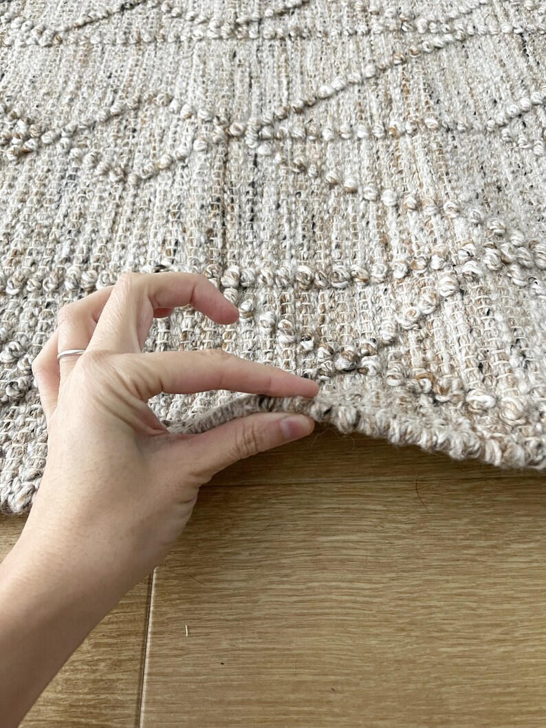 May include: Close-up of a beige and brown woven rug with a textured surface. The rug has a diamond pattern and is made of natural fibers.