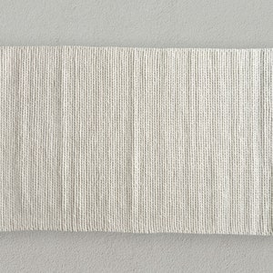 The rug's chunky, soft wool construction adds warmth and texture to the space. Its thick, off-white design perfectly complements the room's sleek, contemporary furnishings.