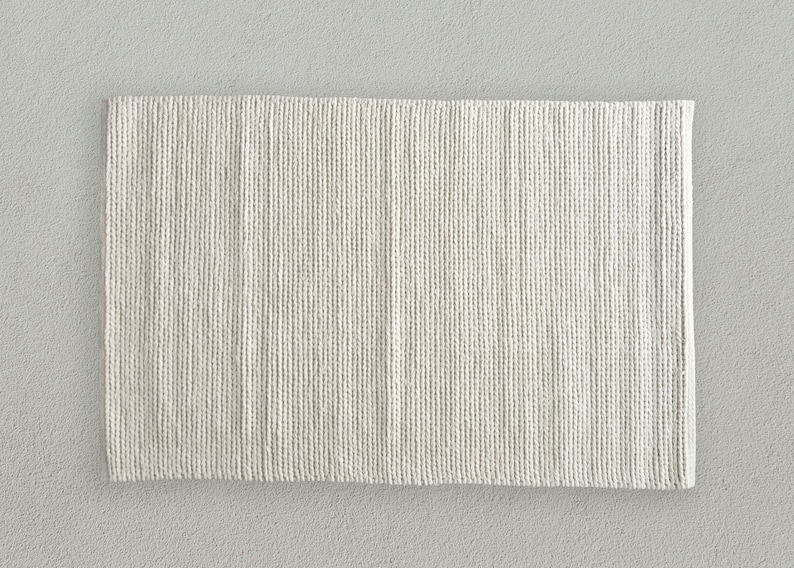 The rug's chunky, soft wool construction adds warmth and texture to the space. Its thick, off-white design perfectly complements the room's sleek, contemporary furnishings.