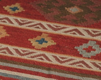 May include: A red, brown, and blue patterned rug with a geometric design. The rug has a fringe border.