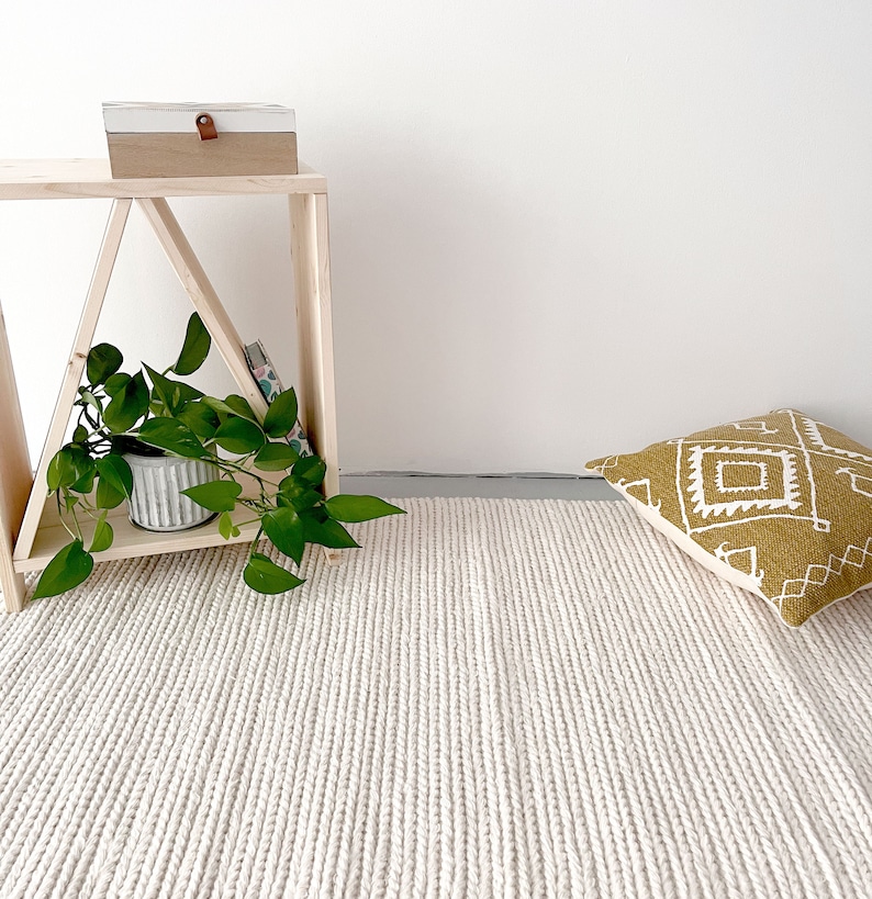 A spacious living room featuring a hand-woven wool flatweave rug. The rug is ivory, with a chunky knit pattern that creates a pebble-like texture. Its thick, soft wool enhances the cozy atmosphere, complementing the room's modern decor.