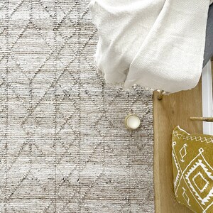May include: A white throw blanket draped over a chair, with a beige and brown patterned rug underneath. A small candle and a yellow throw pillow with a geometric pattern are on the floor.