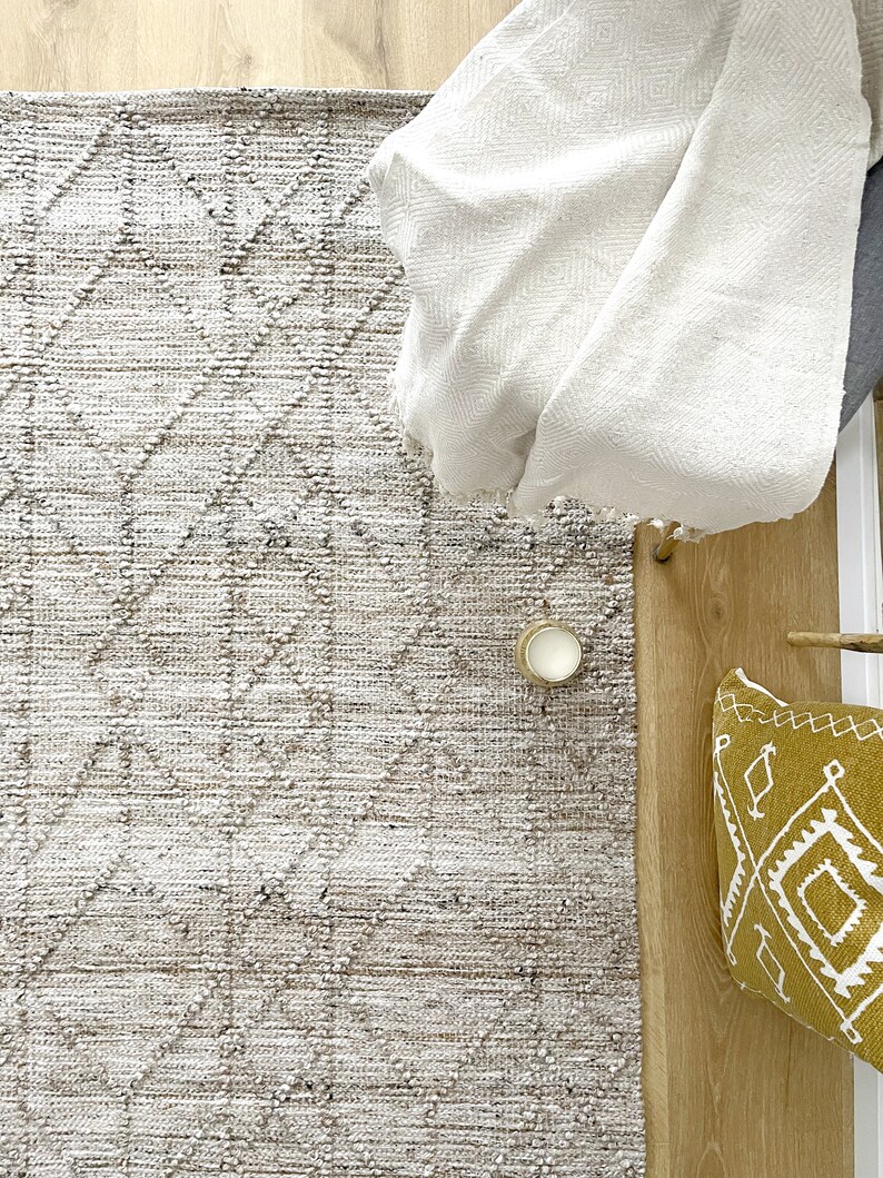 May include: A white throw blanket draped over a chair, with a beige and brown patterned rug underneath. A small candle and a yellow throw pillow with a geometric pattern are on the floor.