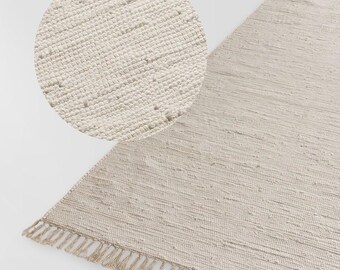 May include: A beige woven rug with a fringe border. The rug has a textured surface and is made of natural fibers.