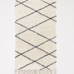 May include: A white and black diamond patterned rug with fringe on all sides.