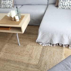 A light gray sectional sofa with a white throw blanket on the chaise lounge. The sofa is sitting on a natural jute rug with a light wood coffee table in front of it. The coffee table has a woven placemat and a vase with white flowers and candles on it.