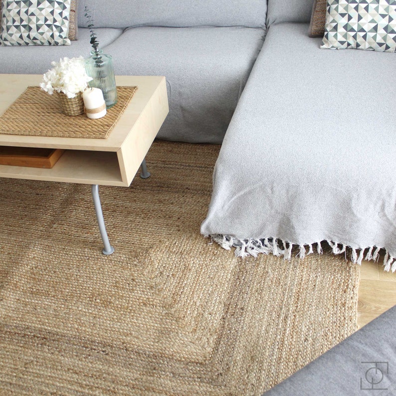 A light gray sectional sofa with a white throw blanket on the chaise lounge. The sofa is sitting on a natural jute rug with a light wood coffee table in front of it. The coffee table has a woven placemat and a vase with white flowers and candles on it.