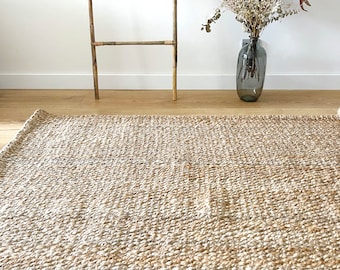 May include: A natural fiber rug with a woven texture in a light beige color. The rug is made of jute and has a subtle sheen.