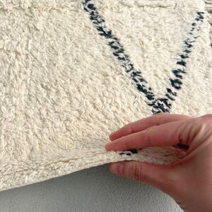 May include: A white fluffy rug with black geometric designs. The rug is folded in half and a hand is holding the edge of the rug.