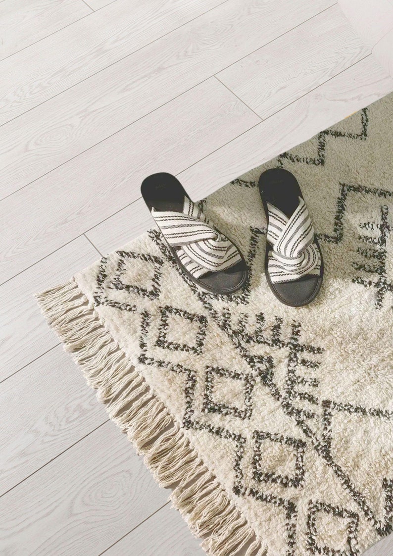 May include: A pair of black and white striped slippers with a knotted design on a white and black patterned rug with fringe.