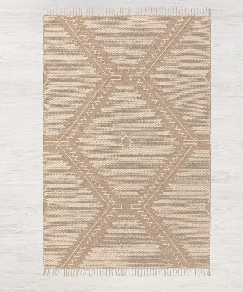 Peut inclure: Un tapis beige avec un motif g&eacute;om&eacute;trique blanc. Le tapis a une bordure en franges.