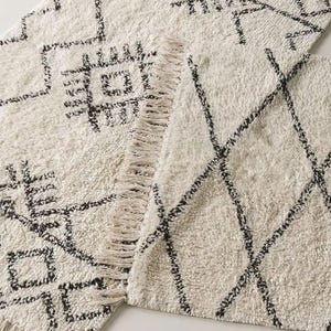 May include: Two white and black patterned rugs with fringe edges. The rugs have geometric designs.