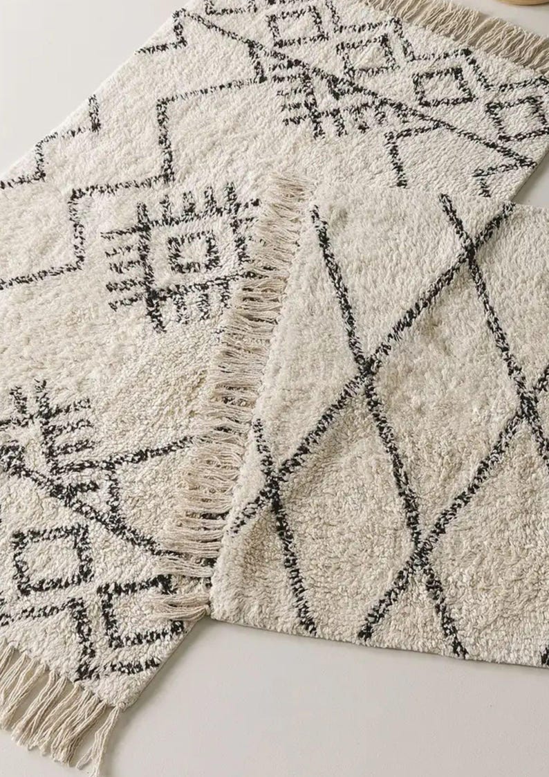 May include: Two white and black patterned rugs with fringe edges. The rugs have geometric designs.