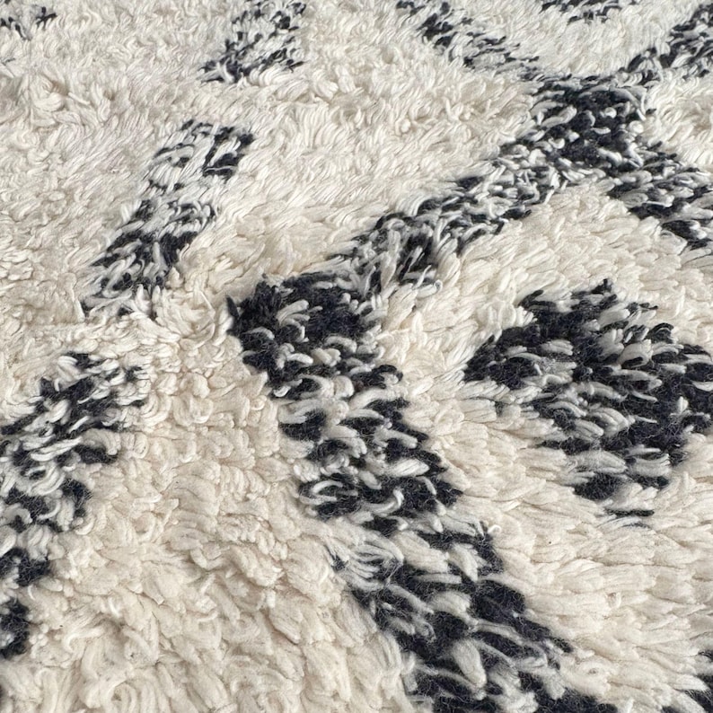 May include: Close-up of a white and black patterned rug with a soft, fluffy texture. The rug has a geometric design with black lines and white spaces.