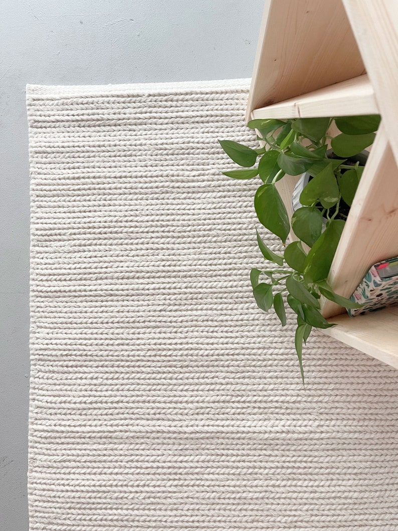 A Scandinavian-style sitting area with a hand-knotted chunky wool rug. The rug's ivory hue and pebble-like texture offer a soft, inviting touch. The thick, plain off-white design is both stylish and functional, enhancing the room's minimalist appeal.