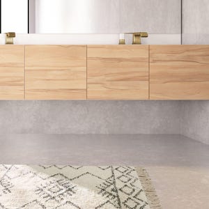 May include: A white bathroom vanity with a wooden cabinet and a white countertop. The vanity has two gold faucets and a white rug with a black geometric pattern is on the floor.