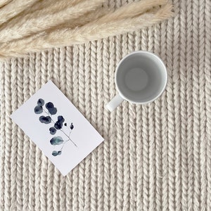 An elegant ivory chunky knit wool area rug displayed in a bedroom. The rug's hand-knotted, felted wool design provides a plush underfoot feel. Its plain off-white color seamlessly blends with the contemporary, Scandinavian-inspired interior.