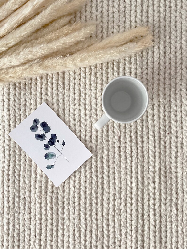 An elegant ivory chunky knit wool area rug displayed in a bedroom. The rug's hand-knotted, felted wool design provides a plush underfoot feel. Its plain off-white color seamlessly blends with the contemporary, Scandinavian-inspired interior.