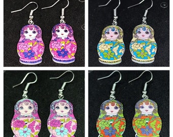 May include: Four pairs of Matryoshka doll earrings. Each pair features a different color scheme, including pink, blue, and orange. The earrings have silver-colored hooks and are decorated with floral patterns and doll faces.