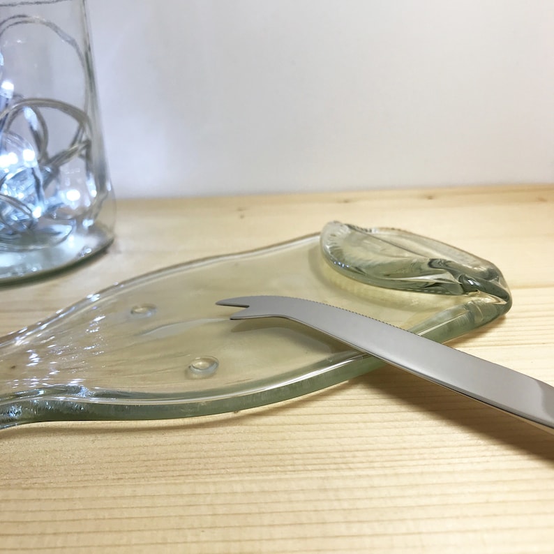 May include: A clear glass cheese board made from a recycled wine bottle with a silver cheese knife.