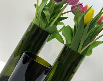 May include: Two dark green glass vases with a bouquet of purple, pink, yellow, and white tulips.