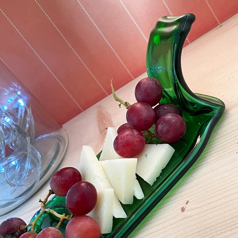 May include: A green glass bottle cut and shaped into a serving dish, filled with red grapes and white cheese wedges.