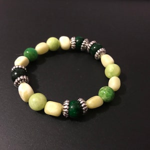 May include: A green and white beaded bracelet with silver accents. The beads are made of jade and are arranged in a gradient pattern.