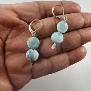 May include: A pair of silver dangle earrings with two round blue and white gemstone beads on each earring.