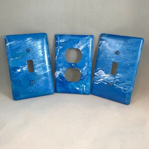 May include: Three blue light switch and outlet covers with a white marbled design. The covers are made of plastic and have a glossy finish.