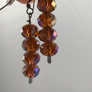 May include: A pair of dangle earrings with a silver tone finish. Each earring features five faceted amber glass beads.